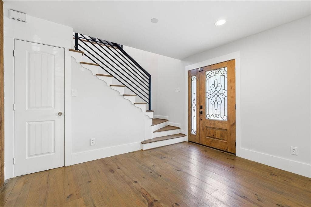 4310 Forest Bend Road, Dallas, TX 75244 Entryway featuring wood-finish flooring, a wood-panel front door with decorative ironwork and sidelights, a staircase with wood treads and a black metal railing, a white paneled door, and recessed lighting