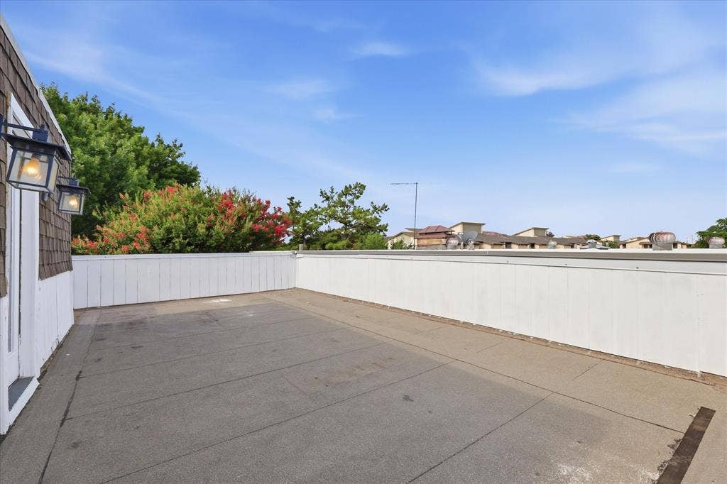 4310 Forest Bend Road, Dallas, TX 75244 Rooftop deck featuring a protective perimeter wall, two exterior wall sconces, and a textured roofing surface