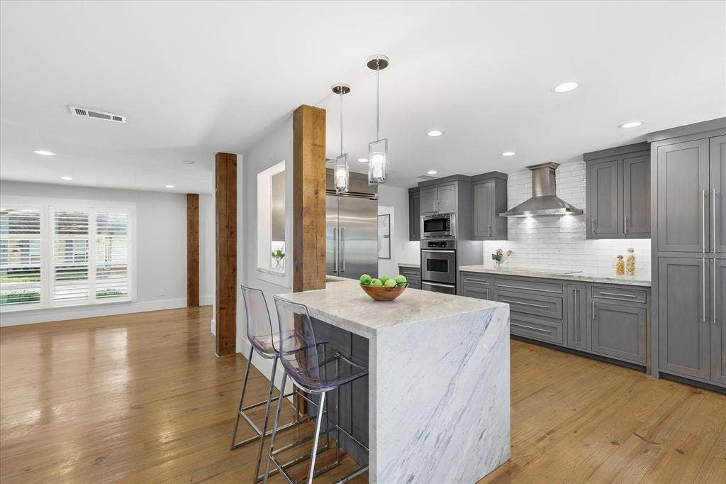 4310 Forest Bend Road, Dallas, TX 75244 Open-concept kitchen featuring an oversized island with waterfall-edge countertop, grey cabinetry, stainless steel appliances, and wood-finish flooring