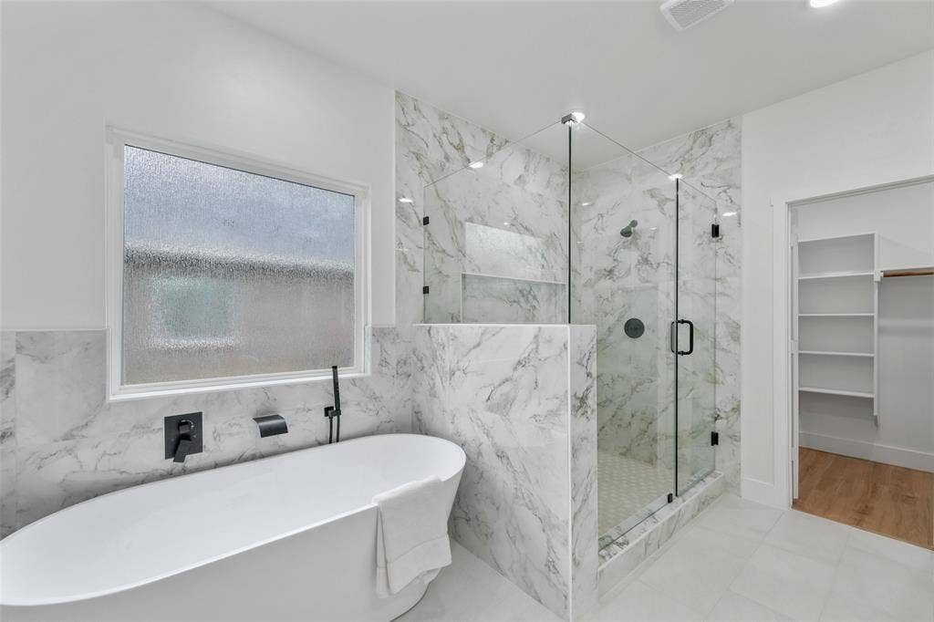 117 Parkside Drive, Trinidad, TX 75163 Bathroom featuring a freestanding soaking tub with matte black fixtures, a spacious glass-enclosed shower with marble-patterned tile, and light-colored flooring