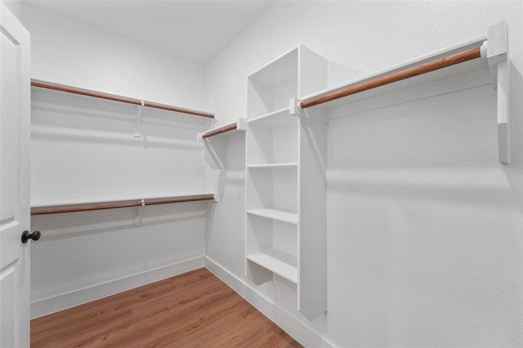 117 Parkside Drive, Trinidad, TX 75163 Walk-in closet featuring wood-finish flooring, white built-in shelving, two levels of hanging rods, and a white six-panel door with black hardware