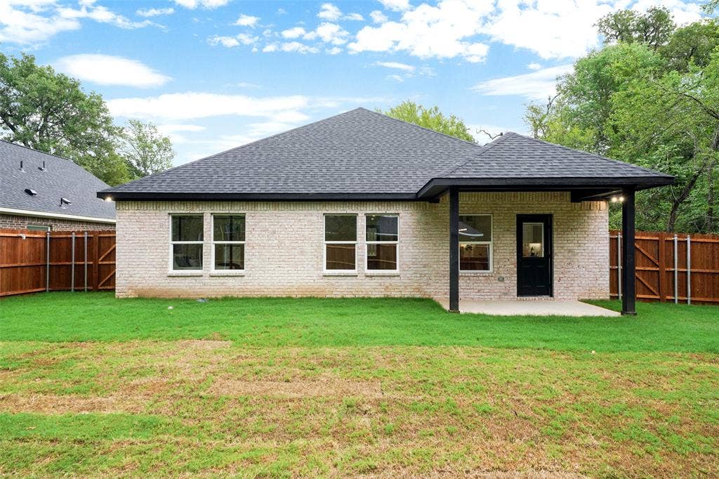 117 Parkside Drive, Trinidad, TX 75163 Rear exterior featuring light-colored brick siding, a dark shingle roof, a covered patio with dark support beams, and a dark exterior door