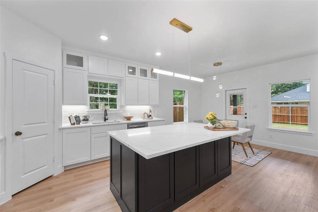 117 Parkside Drive, Trinidad, TX 75163 Modern kitchen featuring a large central island with a solid surface countertop, white cabinetry with upper glass-front accents, wood-finish flooring, and recessed lighting
