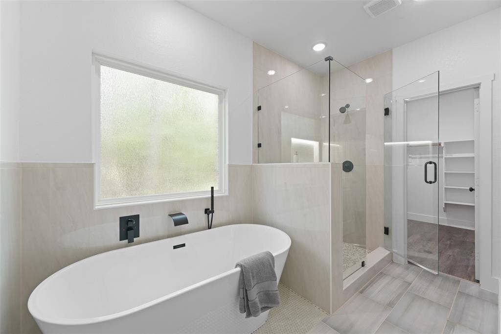 122 E Beachwood Loop, Trinidad, TX 75163 Contemporary bathroom featuring a freestanding soaking tub with matte black fixtures, a spacious glass-enclosed shower with tiled walls and pebble flooring, and large format floor tiling