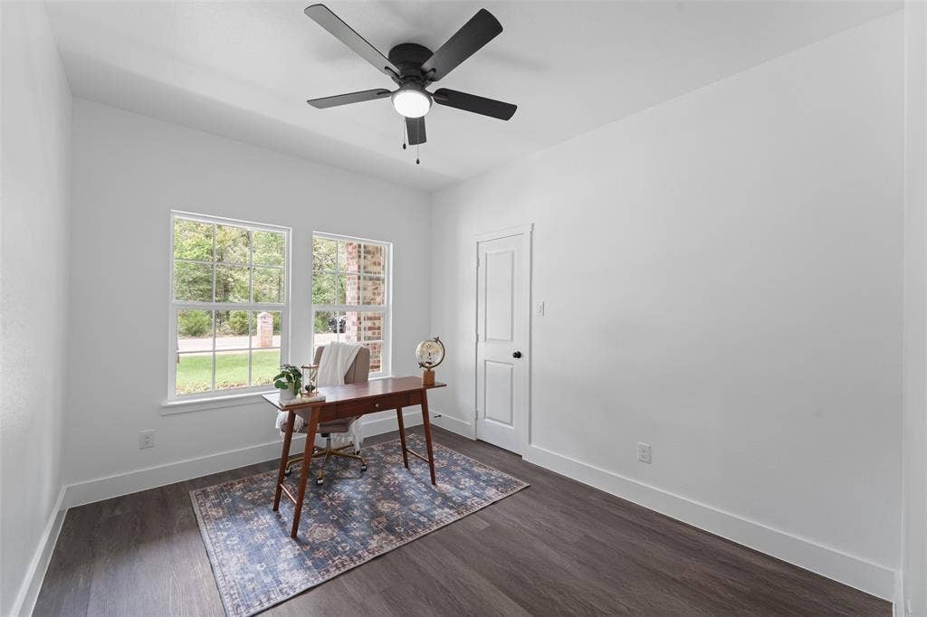 122 E Beachwood Loop, Trinidad, TX 75163 Bright room featuring two large windows, dark wood-finish flooring, a modern black ceiling fan with integrated lighting, a white paneled door, and crisp white walls