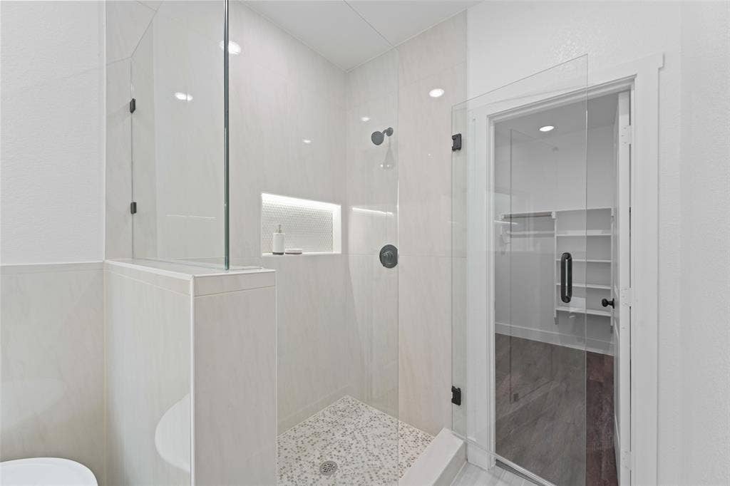 122 E Beachwood Loop, Trinidad, TX 75163 Walk-in shower featuring a frameless glass enclosure, tiled walls, built-in shelving with accent lighting, dark-finish fixtures, and a pebble-mosaic floor