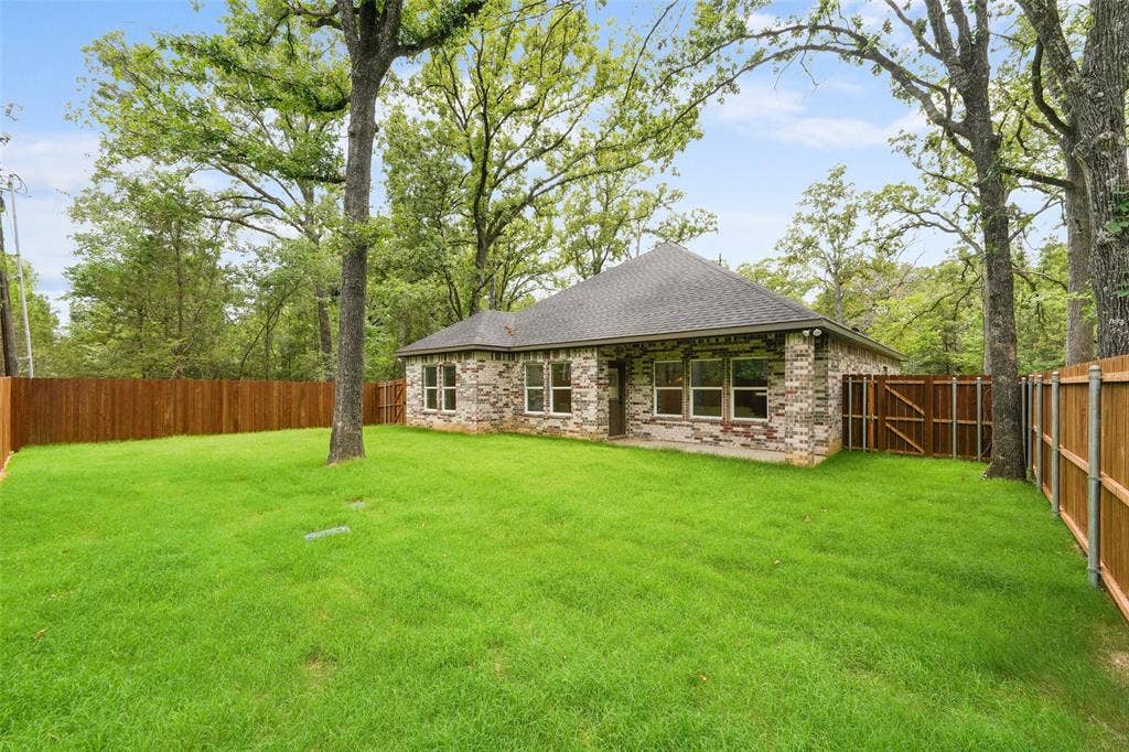 122 E Beachwood Loop, Trinidad, TX 75163 Expansive rear yard featuring a manicured lawn, full privacy fencing, and mature trees