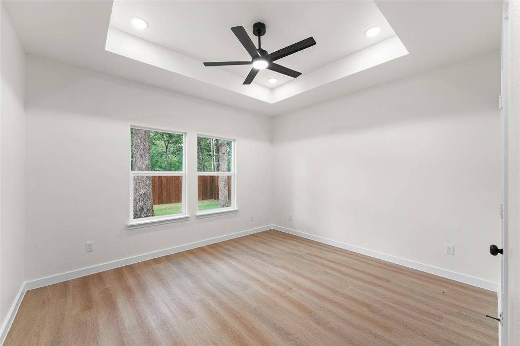 231 E Beachwood Loop, Trinidad, TX 75163 Spacious room featuring a tray ceiling with recessed lighting, a contemporary black ceiling fan, two windows providing natural light, wood-finish flooring, and crisp white trim