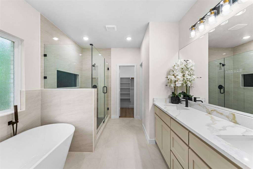 231 E Beachwood Loop, Trinidad, TX 75163 Spacious bathroom featuring a freestanding soaking tub with a wall-mounted faucet, a glass-enclosed shower with a recessed niche, a double vanity with a marble-finish countertop, and a large mirror with overhead lighting