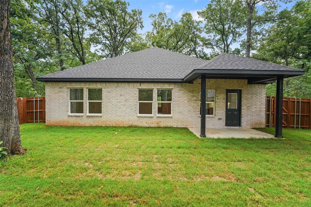 231 E Beachwood Loop, Trinidad, TX 75163 Rear facade featuring light-colored brick, a covered concrete patio, and a dark asphalt shingle roof