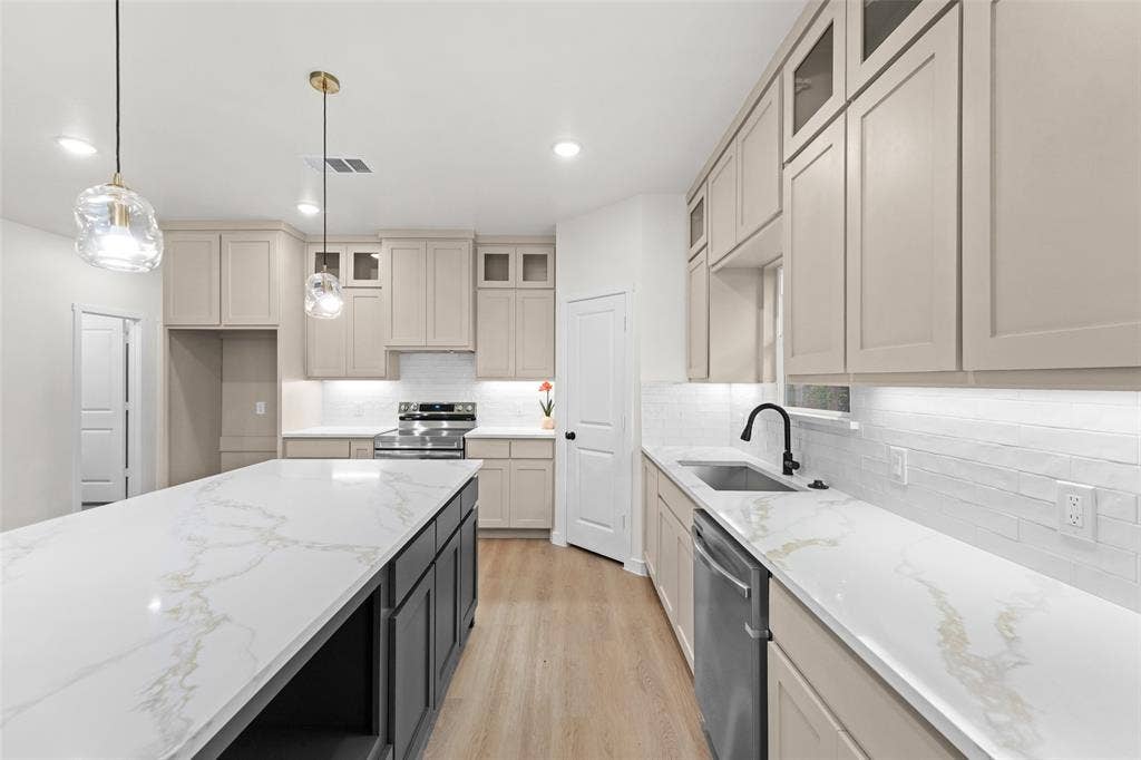 231 E Beachwood Loop, Trinidad, TX 75163 Modern kitchen featuring a large island with a white and gold veined countertop, pendant lighting, light-toned cabinetry, stainless steel appliances, and wood-finish flooring