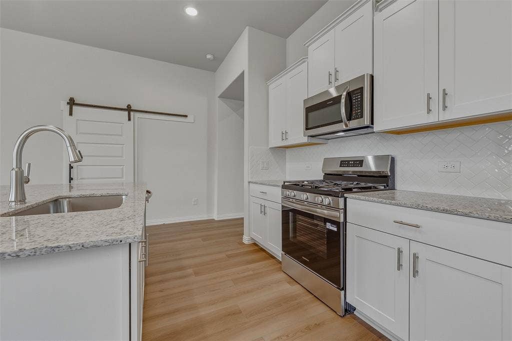 White cabinetry, stainless steel appliances, granite countertops, wood-finish flooring, and a barn door entry
