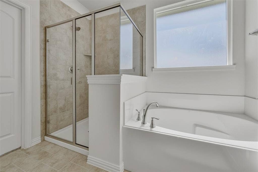 Built-in soaking tub with chrome fixtures, enclosed shower with floor-to-ceiling tile, and a frosted window