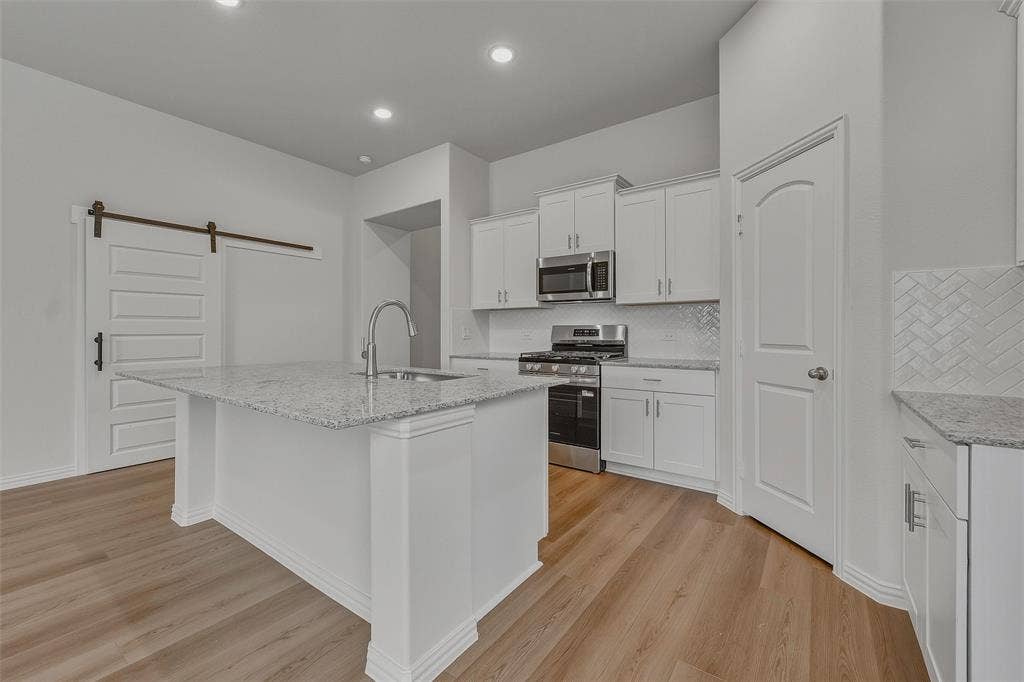 Kitchen featuring wood-finish flooring, recessed lighting, white cabinetry, a kitchen island with a sink, and stainless steel appliances