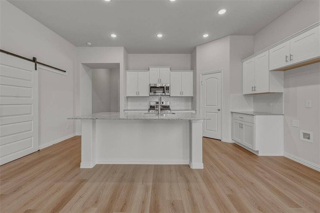 Kitchen featuring a central island with a light-toned countertop, white cabinetry with silver-toned hardware, stainless steel microwave, and wood-finish flooring