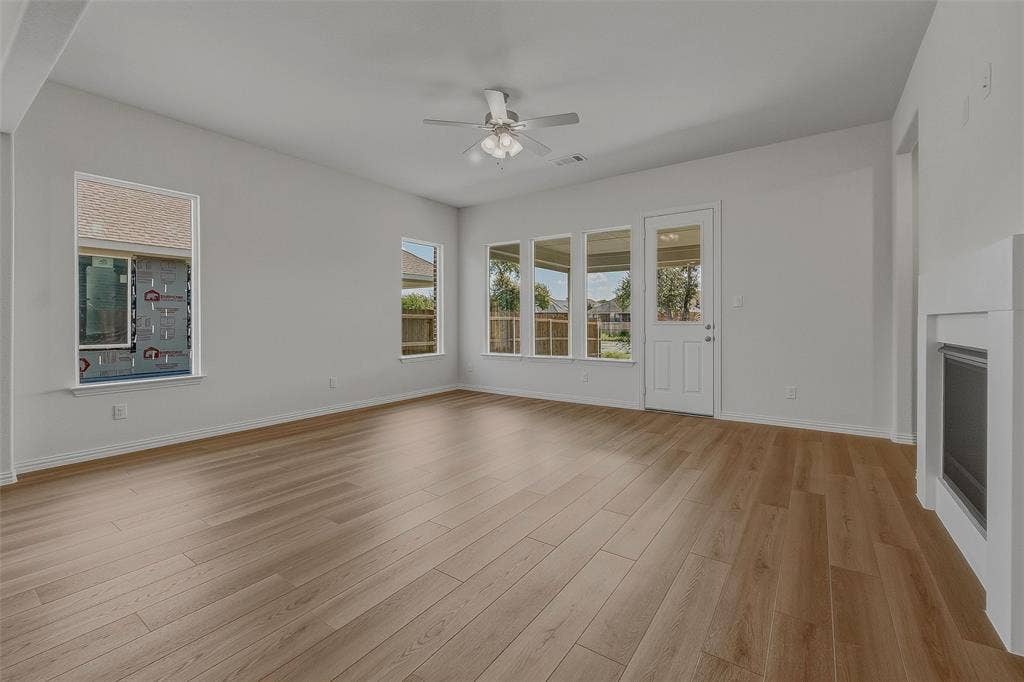 Spacious room featuring light wood-finish flooring, multiple windows, a ceiling fan, and a built-in fireplace