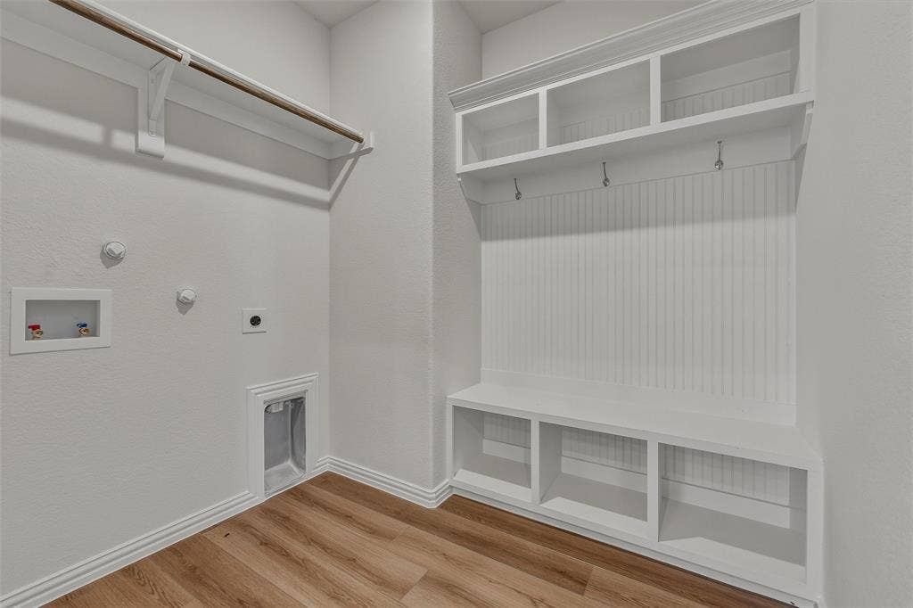 Laundry area featuring wood-finish flooring, built-in coat rack, built-in bench, integrated storage cubbies, and overhead shelving