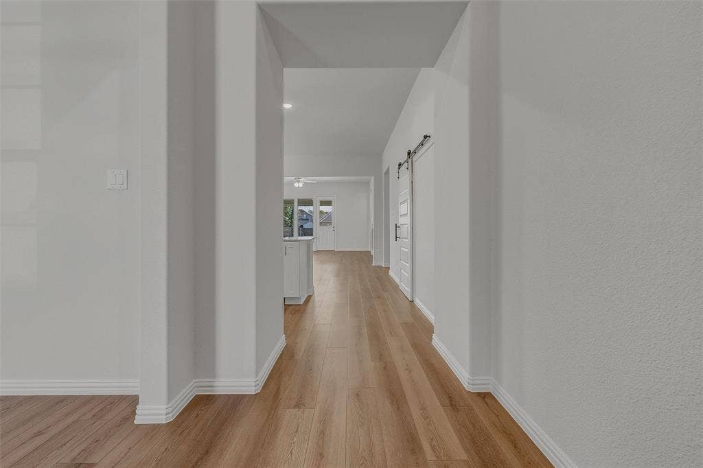 Wood-finish flooring throughout, white interior walls, and a sliding barn door with black hardware