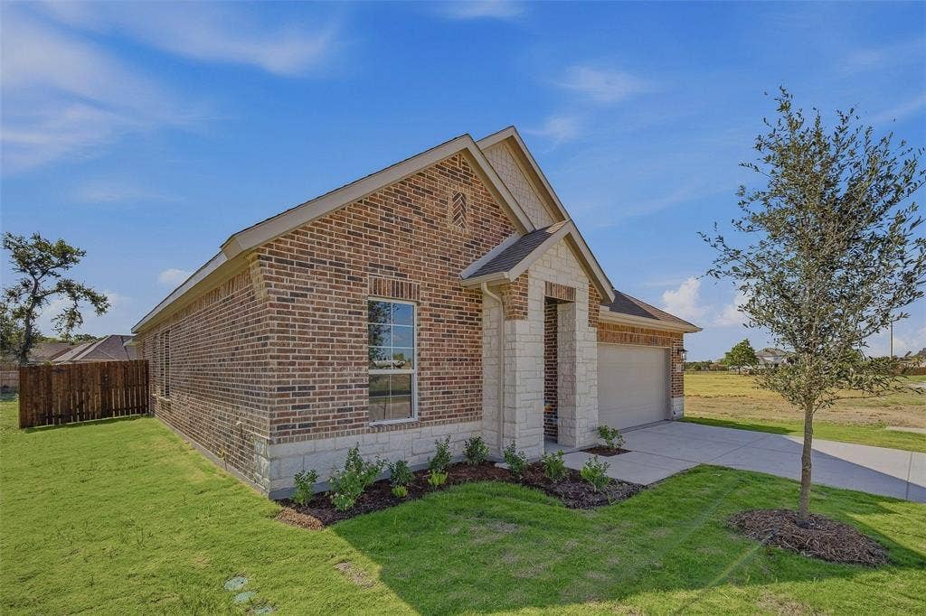 Brick exterior with stone accents, attached garage, concrete driveway, and manicured lawn