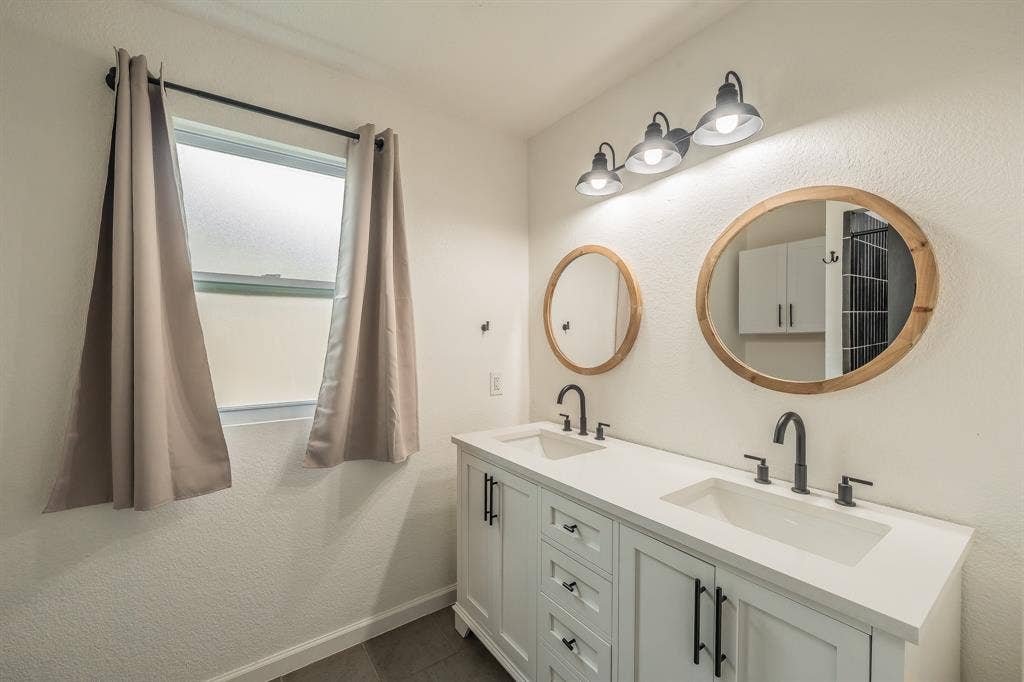 5612 Macgregor Drive, Haltom City, TX 76148 Dual vanity featuring white shaker cabinetry, matte black hardware, integrated sinks, and matching wood-frame mirrors