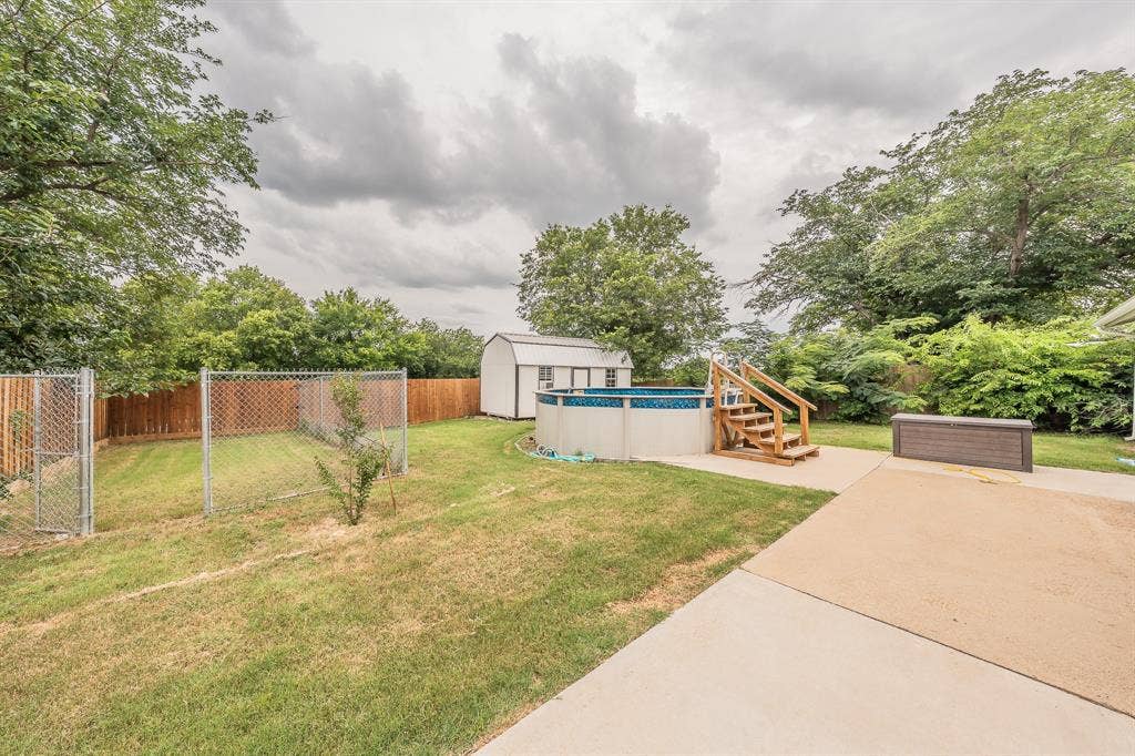 5612 Macgregor Drive, Haltom City, TX 76148 Expansive backyard featuring a fenced-in area, an above-ground swimming pool with wooden steps, a storage shed, a concrete patio, and a wood privacy fence