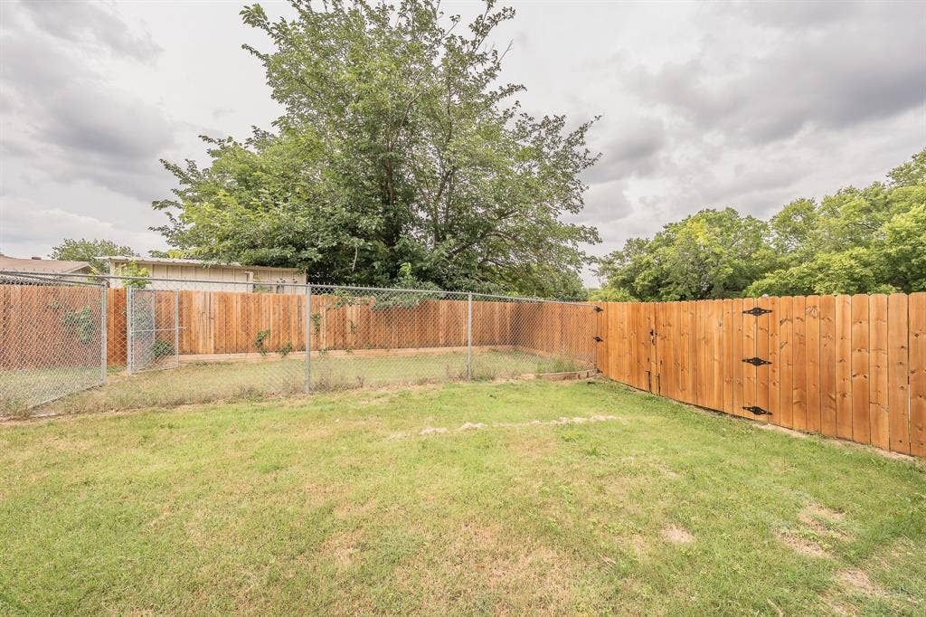 5612 Macgregor Drive, Haltom City, TX 76148 Expansive backyard featuring a combination of chain-link and wood privacy fencing, a mature tree, and a wooden gate with decorative hardware
