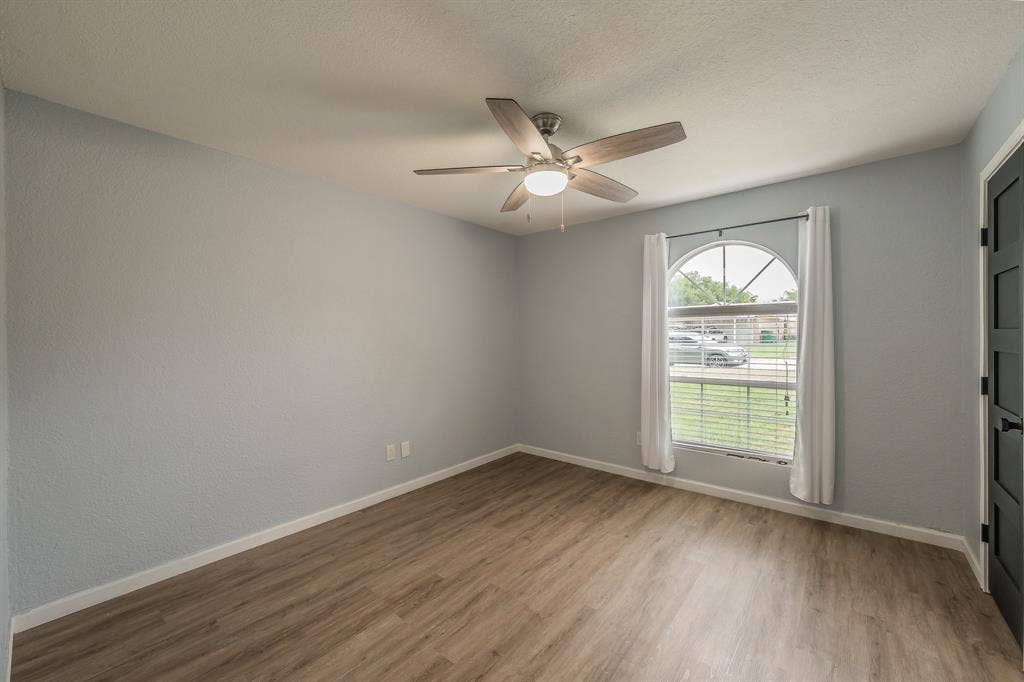 5612 Macgregor Drive, Haltom City, TX 76148 Room featuring wood-finish flooring, a contemporary ceiling fan with integrated lighting, and an arched window with blinds and white curtains
