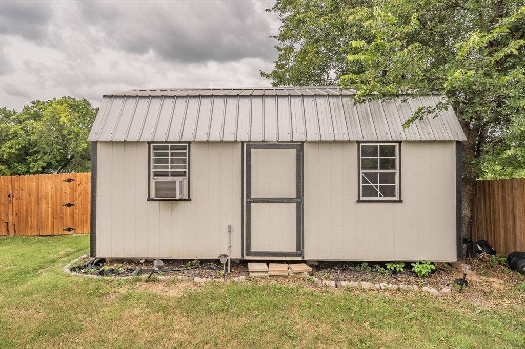 5612 Macgregor Drive, Haltom City, TX 76148 Detached shed featuring a metal gambrel roof, two windows, and AC unit.