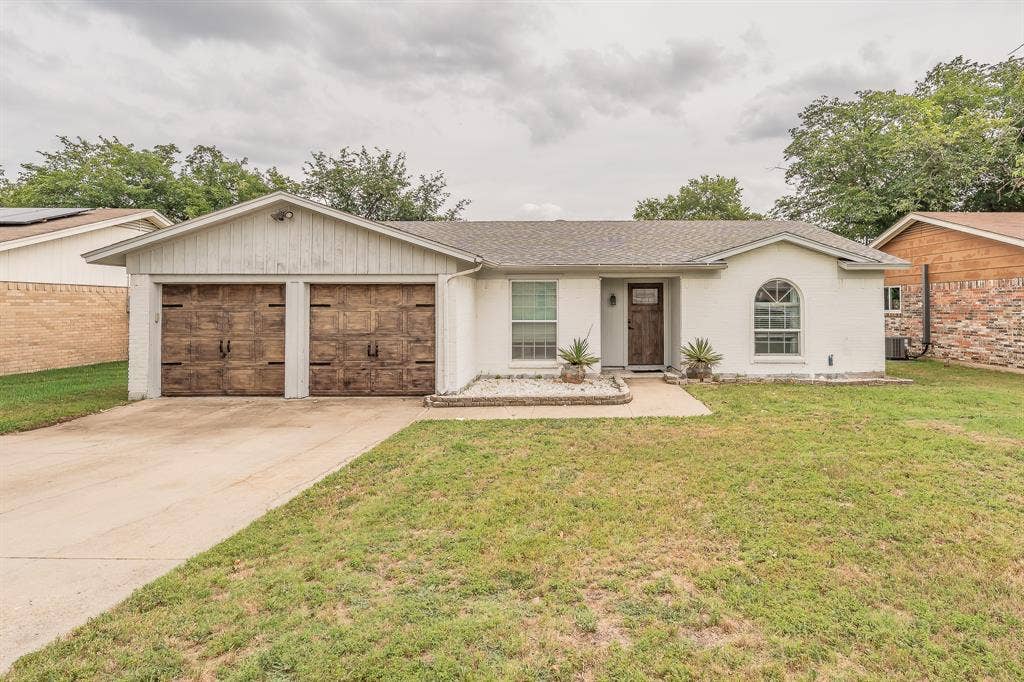 5612 Macgregor Drive, Haltom City, TX 76148 White brick exterior with a contrasting wood-finish front door and two wood-finish garage doors