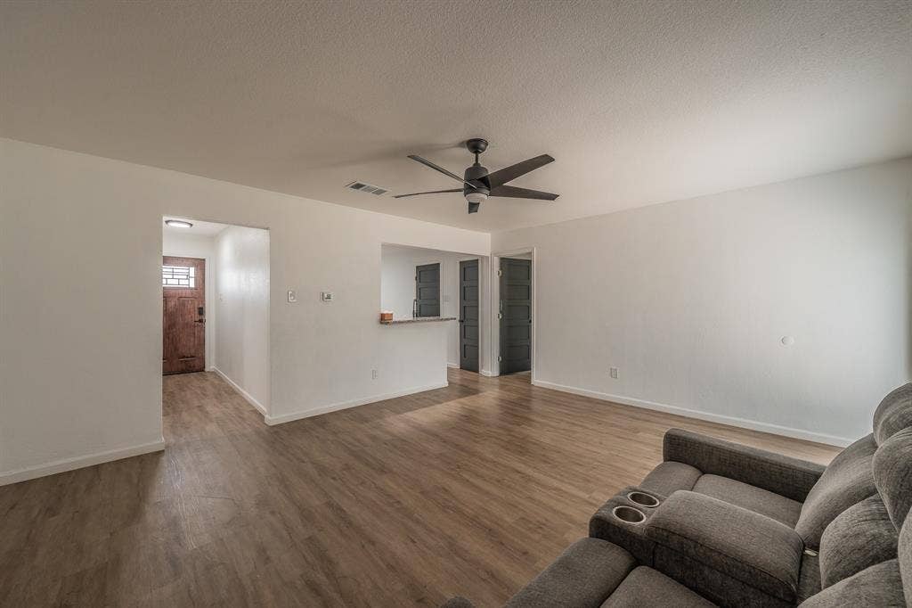 5612 Macgregor Drive, Haltom City, TX 76148 Spacious living area featuring wood-finish flooring, a contemporary ceiling fan with integrated lighting, and crisp white walls