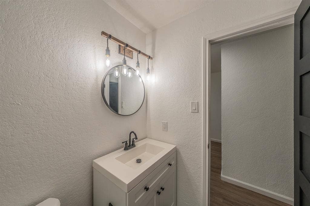 5612 Macgregor Drive, Haltom City, TX 76148 Bathroom vanity featuring a single basin, a dark-toned faucet, and a round mirror