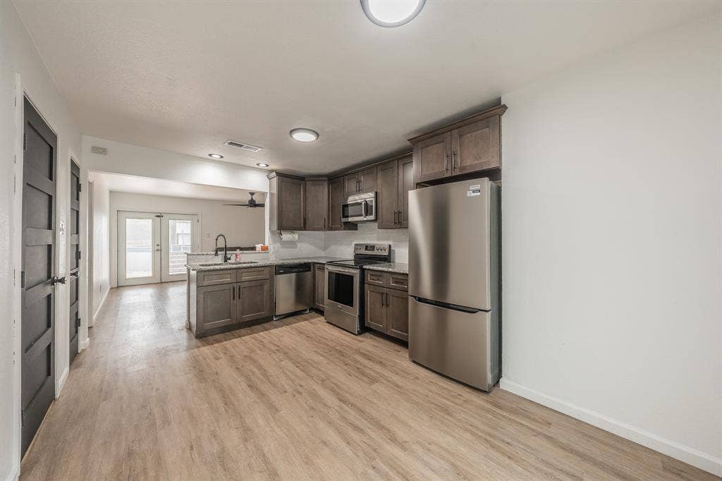 5612 Macgregor Drive, Haltom City, TX 76148 Open-concept kitchen featuring wood-finish flooring, shaker-style cabinetry, stainless steel appliances, and a white subway tile backsplash