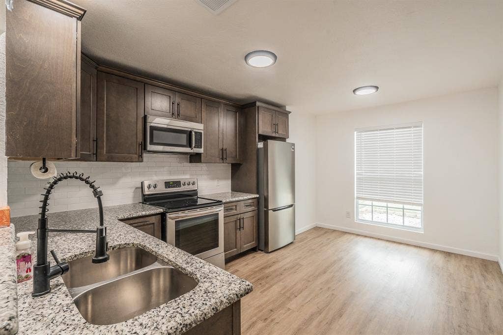 5612 Macgregor Drive, Haltom City, TX 76148 Modern kitchen featuring dark wood cabinetry, speckled countertops, stainless steel appliances, a white subway tile backsplash, and wood-finish flooring