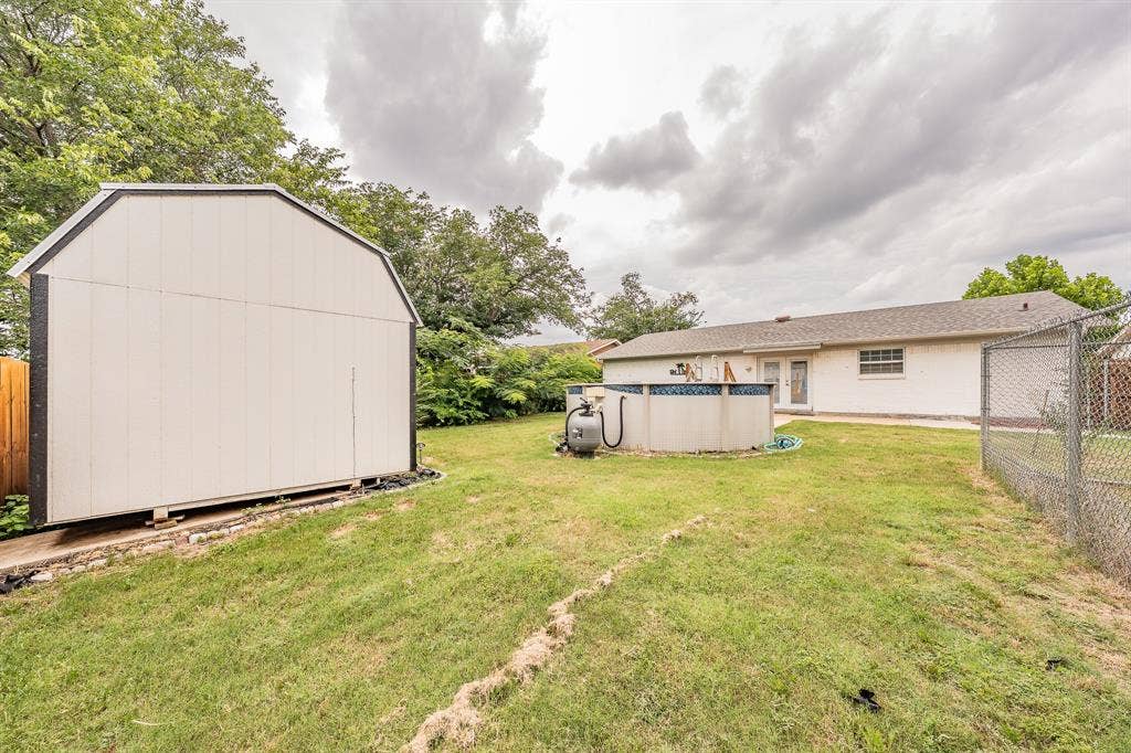 5612 Macgregor Drive, Haltom City, TX 76148 Expansive backyard featuring a gambrel-style storage shed, above-ground swimming pool, and chain-link fencing
