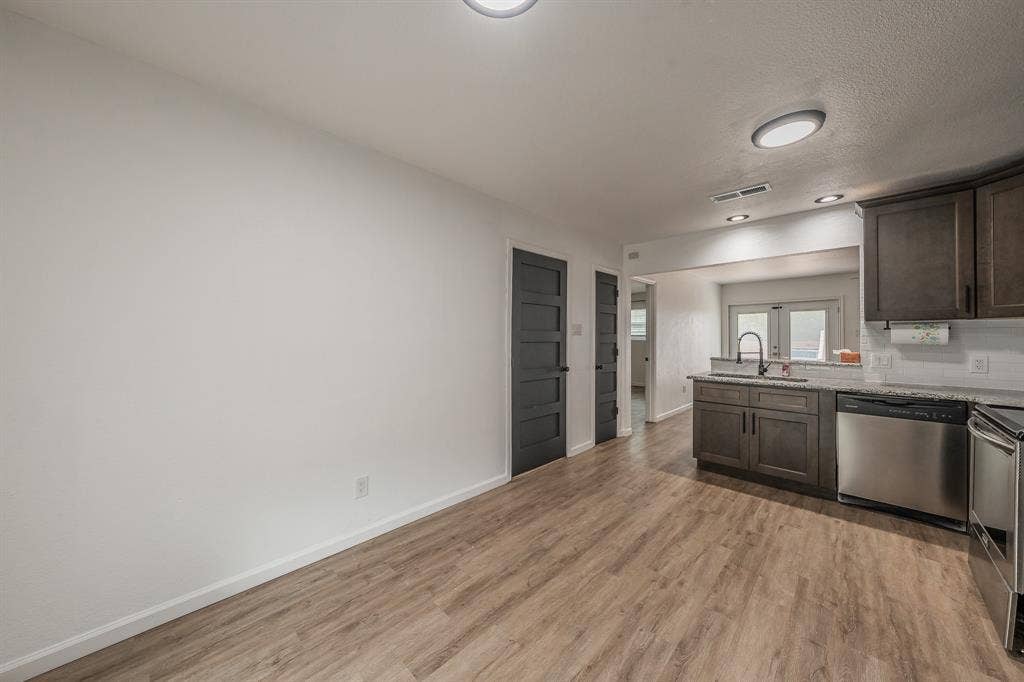 5612 Macgregor Drive, Haltom City, TX 76148 Open-concept kitchen and dining area featuring wood-finish flooring, dark wood cabinetry, stainless steel appliances, a breakfast bar, and white subway tile backsplash