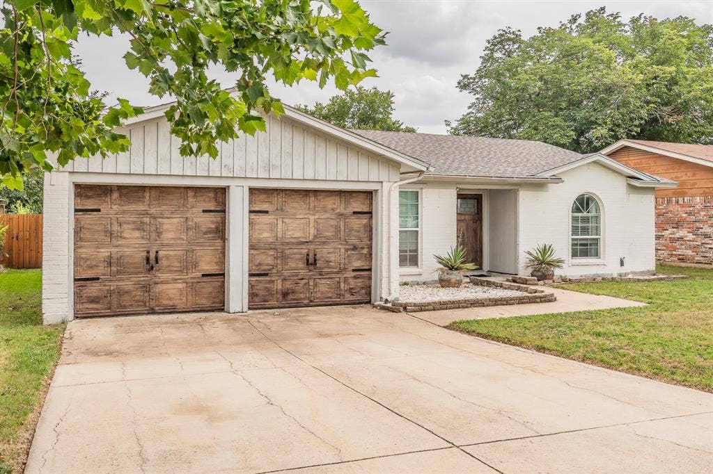 5612 Macgregor Drive, Haltom City, TX 76148 White brick exterior with two wood-finish garage doors