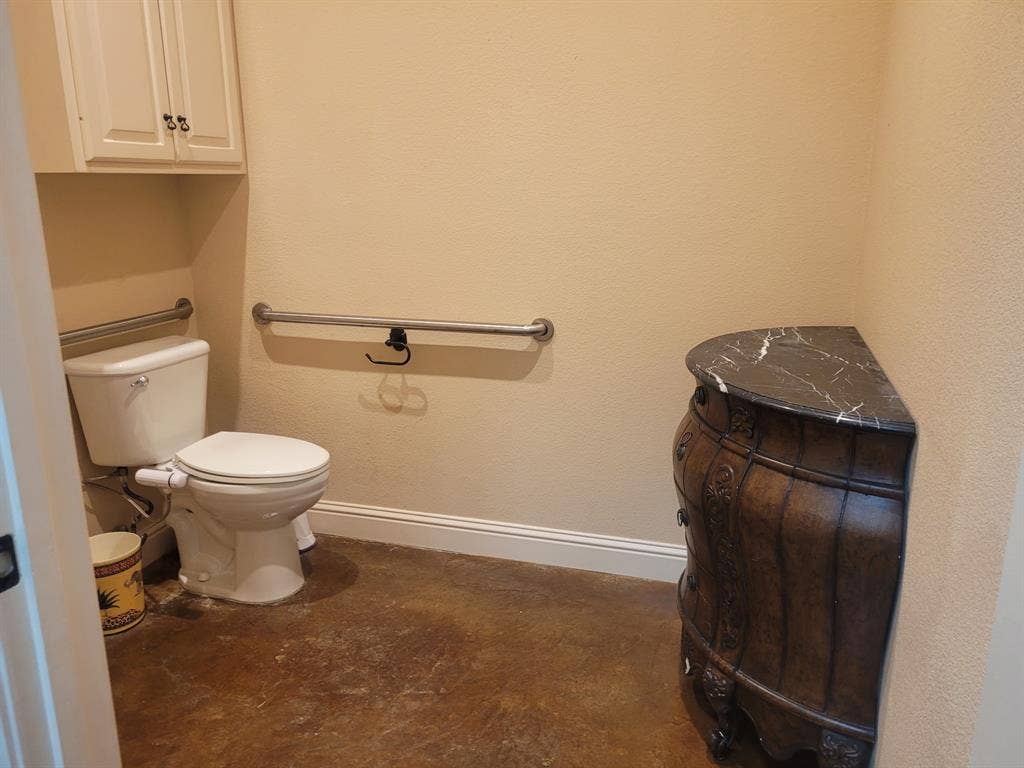 1905 W Ennis Avenue, #301, Ennis, TX 75119 Bathroom featuring a white toilet, support bars, and built-in upper cabinetry with white doors and dark hardware
