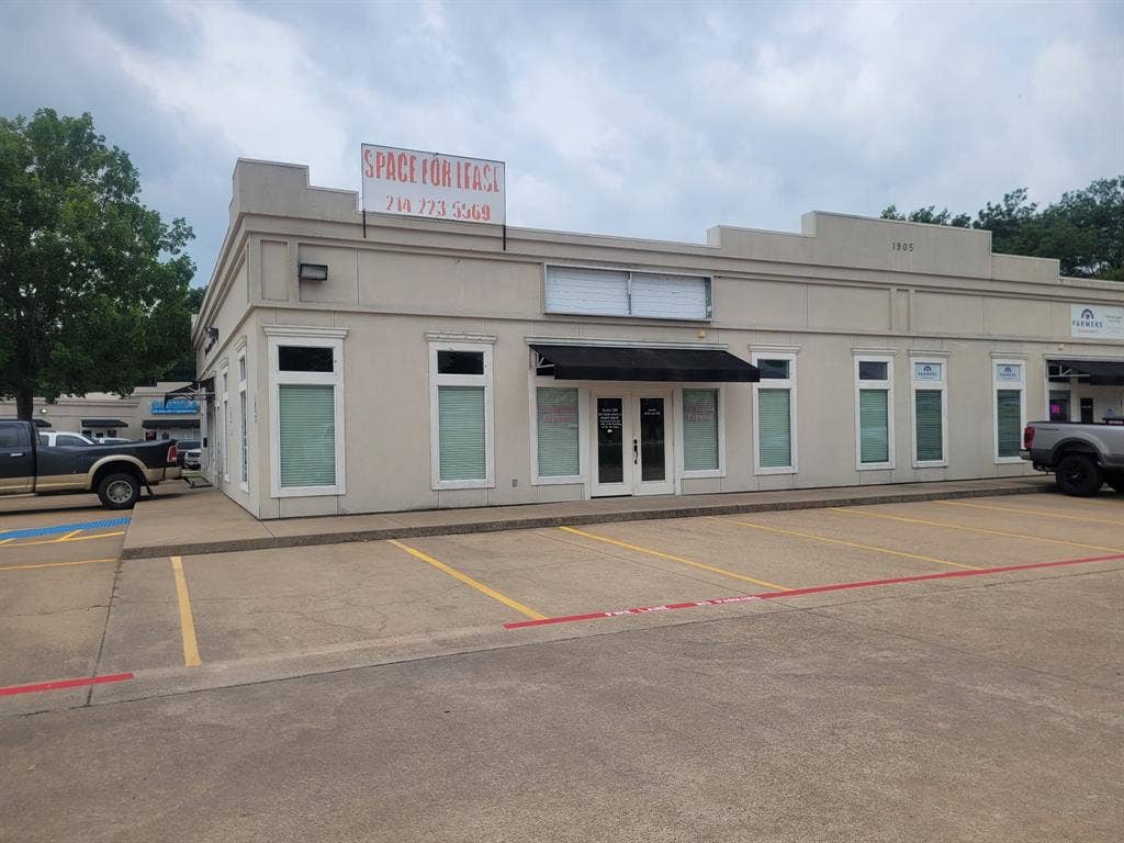 1905 W Ennis Avenue, #301, Ennis, TX 75119 Commercial storefront featuring a recessed entry, prominent black awning, multiple display windows, and a dedicated concrete parking lot with painted space dividers
