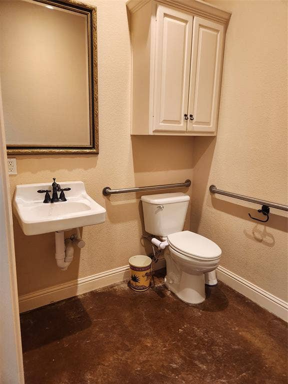 1905 W Ennis Avenue, #301, Ennis, TX 75119 Bathroom featuring a wall-mounted sink with black fixtures, a white toilet, and a framed mirror
