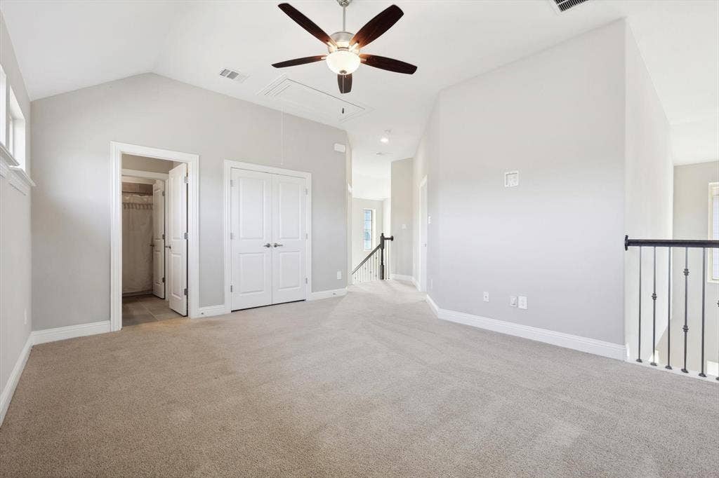 Spacious room featuring vaulted ceilings, a ceiling fan with light fixture, light-toned carpeting, and a double-door closet