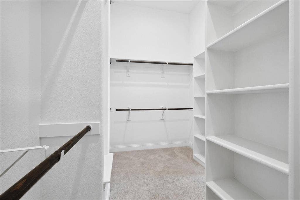 Walk-in closet featuring white wall shelving, multiple hanging rods, and light-toned carpeting