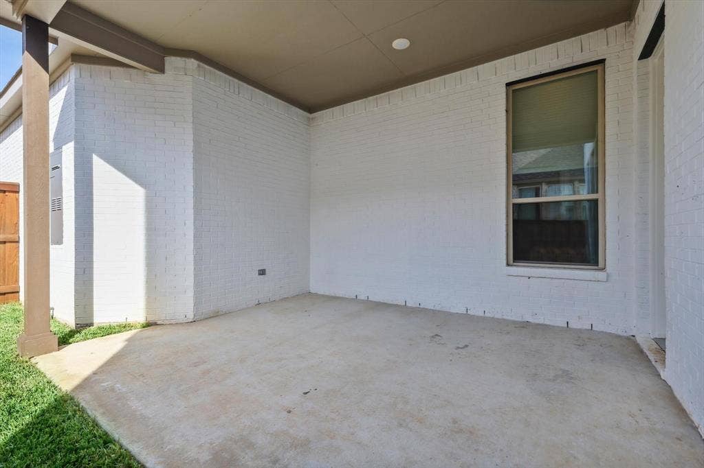 Covered concrete patio with white brick exterior, recessed lighting, and a prominent window