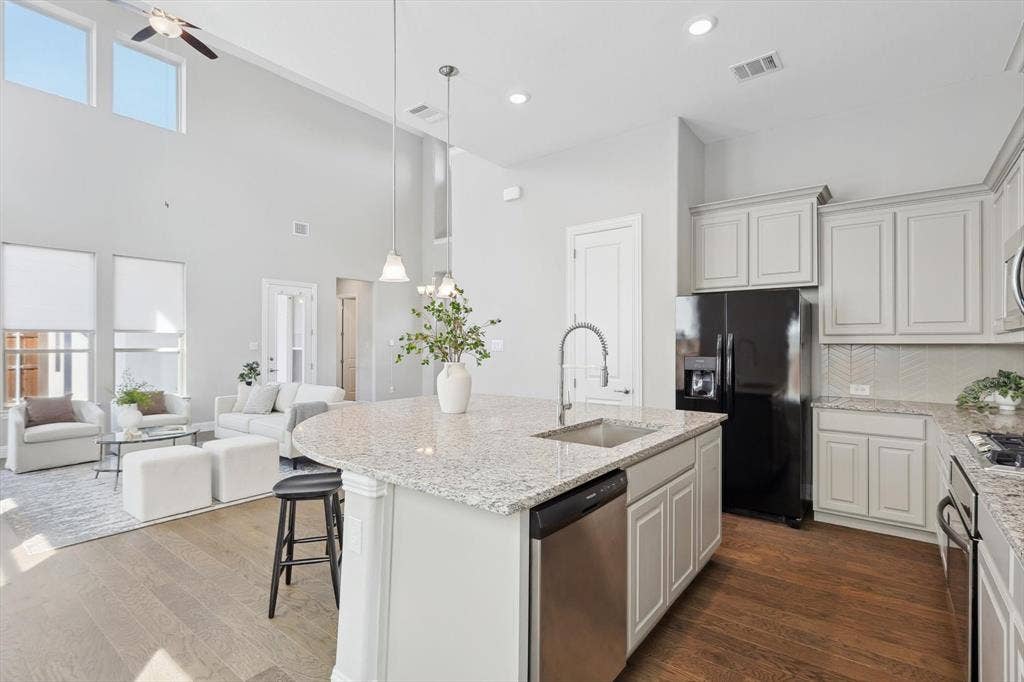 Open-concept living space featuring a kitchen island with integrated sink, wood-finish flooring, soaring ceilings, and abundant natural light from high windows