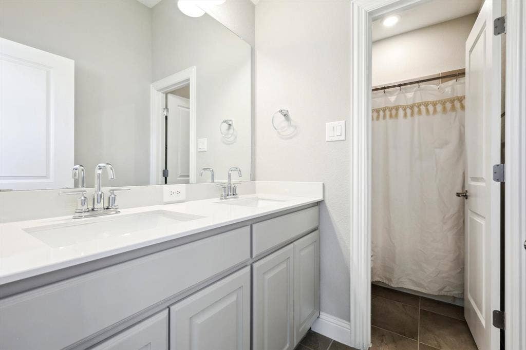 Dual vanity with undermount sinks and chrome faucets, complemented by a large mirror and light gray cabinetry