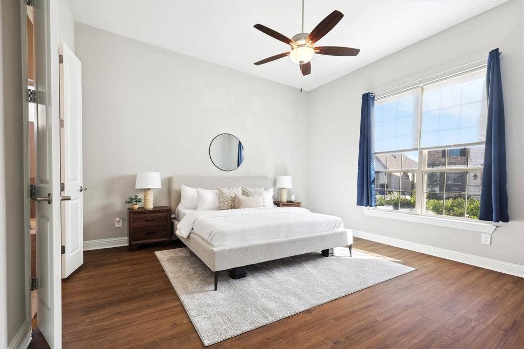 Spacious room featuring wood-finish flooring, a large window with roller shades, high ceilings, and a ceiling fan with integrated lighting