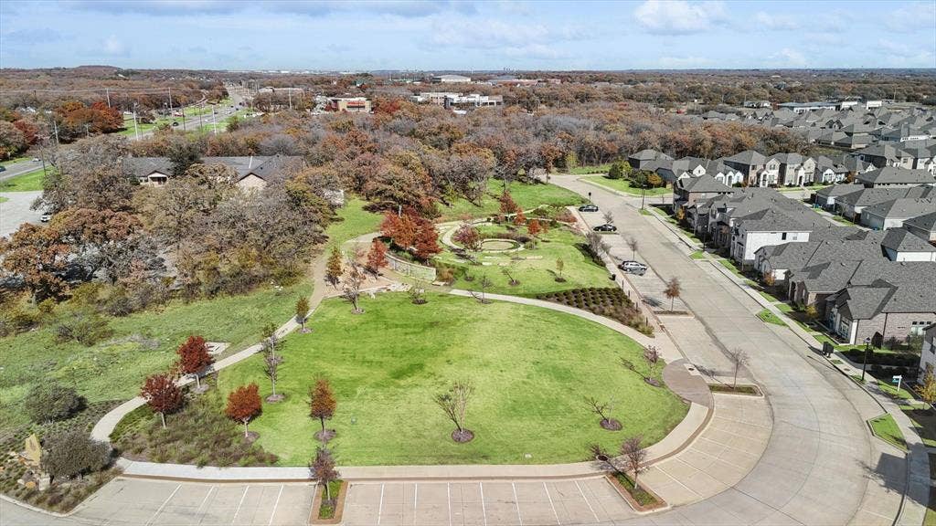 Expansive community park featuring a large green lawn, meandering pathways, mature trees, and a variety of established landscaping