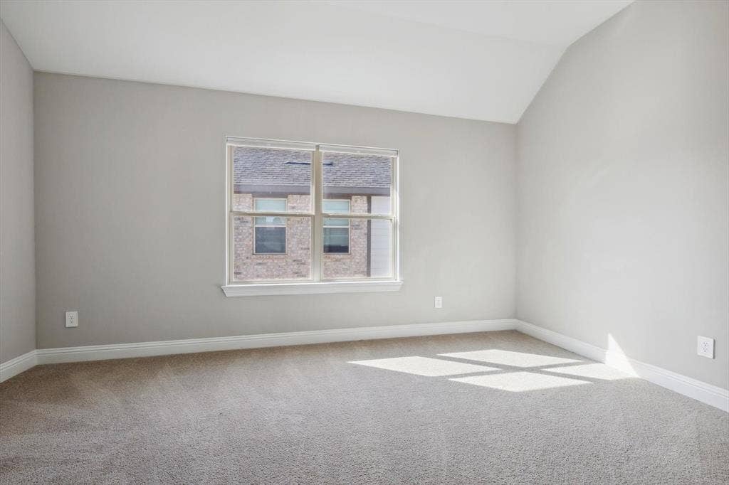 Carpeted interior room featuring a vaulted ceiling and a large window with white trim