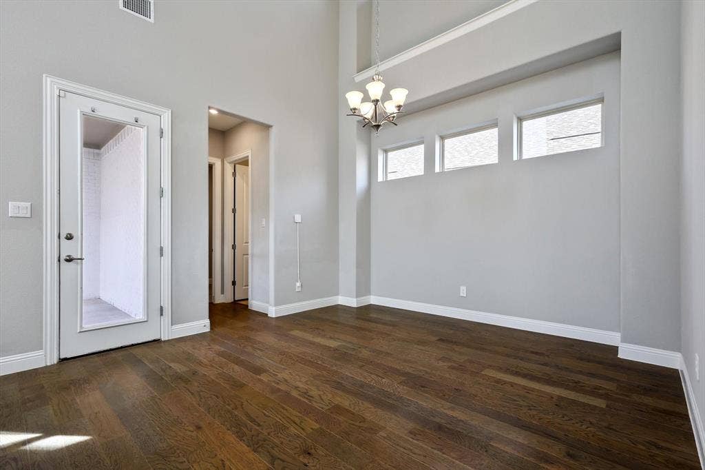 Spacious room featuring vaulted ceilings, rich wood-finish flooring, and a contemporary chandelier