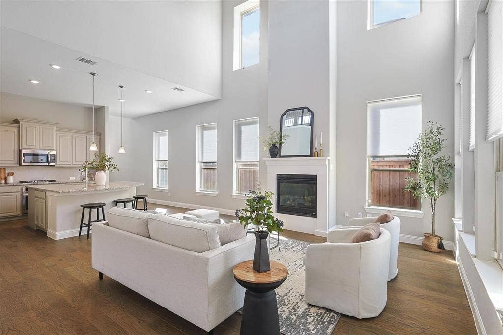 Expansive living area with a fireplace featuring a white mantel, wood-finish flooring, and high ceilings