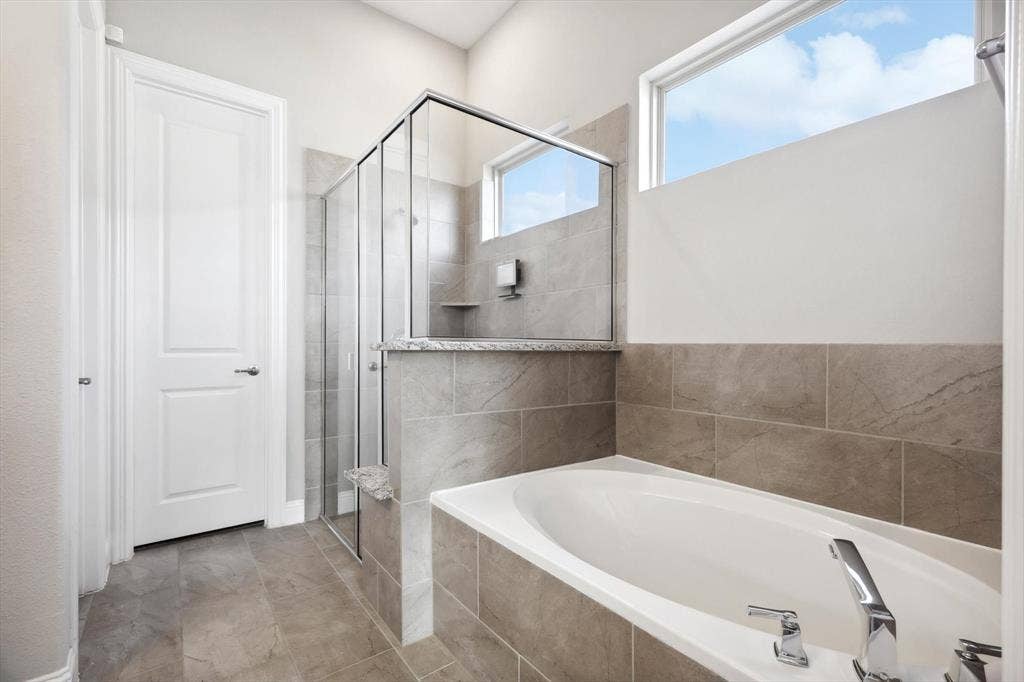 Spacious bathroom featuring a built-in soaking tub, a frameless glass shower enclosure, and large format wall and floor tiling